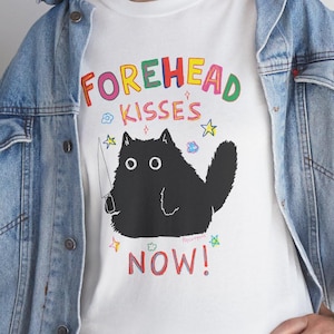May include: White t-shirt with a black cat illustration holding a knife and the text "FOREHEAD KISSES NOW!" in rainbow colors.