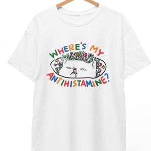 Peut inclure: T-shirt blanc avec un motif coloré d'un chat avec des fleurs sur la tête et le texte "Where's my antihistamine?"