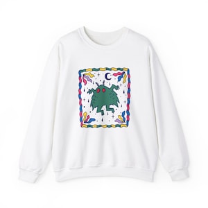 May include: White sweatshirt with a green monster graphic in a colorful frame. The monster has two red eyes and is surrounded by stars, a crescent moon, and raindrops.