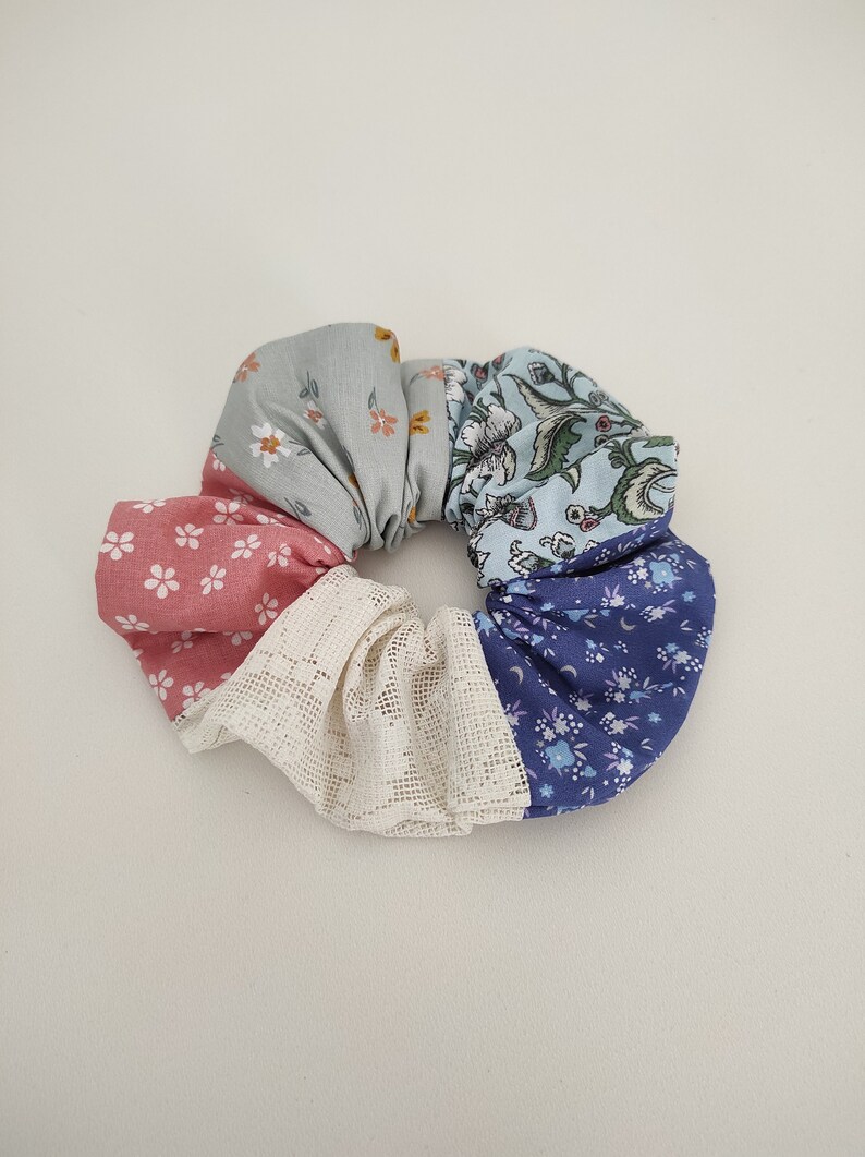 Pu&ograve; includere: Un elastico per capelli in tessuto multicolore con un bordo in pizzo bianco. Lo scrunchie &egrave; realizzato con cinque tessuti diversi con motivi floreali in tonalit&agrave; di blu, rosa e verde.