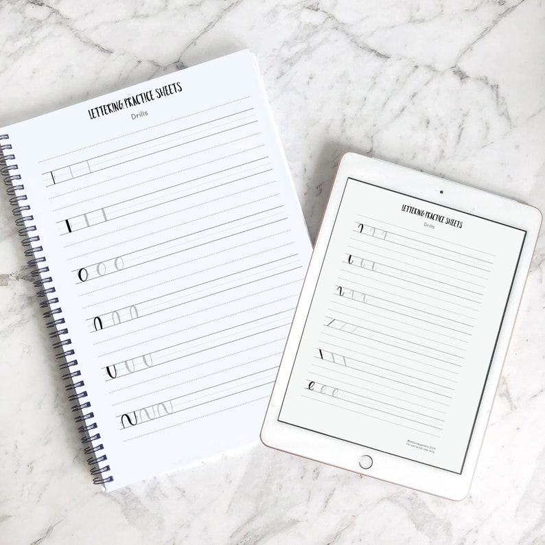 May include: Two white practice sheets for lettering drills. The sheets have lines for practicing different letter strokes. The top sheet is in a bound notebook and the bottom sheet is on a tablet.