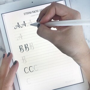 May include: A digital tablet screen displaying a lettering practice sheet with uppercase letters A, B, and C written in cursive. The letters are written in black ink on a white background with gray lines.