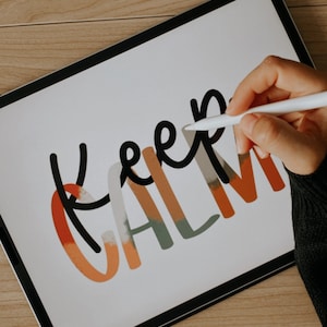 May include: A hand uses a stylus to draw the words "Keep Calm" on a white digital tablet. The words are in black and are outlined in orange, green, and white.