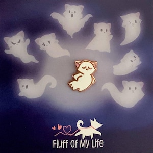 Può includere: Illustrazioni di fantasmi di gatti bianchi su sfondo blu scuro. Al centro c'è una spilla dorata a forma di gatto fantasma. Il testo "Fluff of My Life" è in basso, con un design a forma di gatto e cuore.