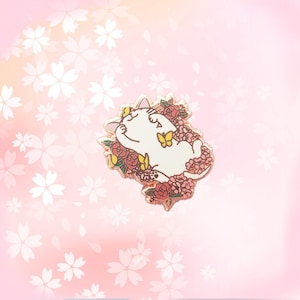 May include: A white cat with pink ears and a pink nose is surrounded by pink and red flowers. The cat is lying on its back with its paws in the air. There are two yellow butterflies near the cat.