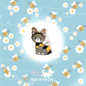 May include: A cute cartoon cat wearing a bee costume with yellow and black stripes, black wings, and a gold crown. The cat is sitting on a white background with a blue and white floral pattern.