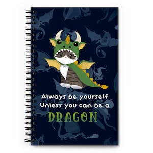 May include: A spiral bound notebook with a dark blue background featuring a cartoon cat wearing a green dragon costume. The text "Always be yourself Unless you can be a DRAGON" is printed in white on the cover.