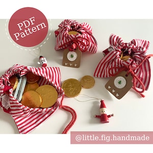 Puede incluir: Tres bolsas de tela a rayas rojas y blancas llenas de monedas de chocolate doradas. Cada bolsa tiene una etiqueta marrón con el texto "Feliz Navidad" y una cinta roja atada alrededor de la parte superior. Las bolsas están sobre una superficie blanca.