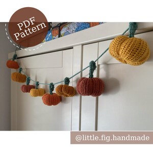 May include: A garland of crocheted pumpkins in various shades of orange and brown, hanging from a white door. The garland is made of a teal string and has a PDF pattern available. The text "@little.fig.handmade" is at the bottom of the image.