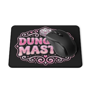 Peut inclure: Un tapis de souris rectangulaire noir avec un motif rose portant le texte "DUNG MAST" et une icône de dé à 20 faces entourée de volutes décoratives et de petits cœurs. Une souris d'ordinateur noire est posée sur le côté droit du tapis.