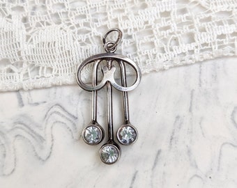 May include: A silver charm with a geometric design and three clear rhinestones hanging from it.