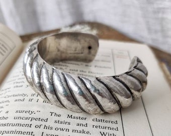 May include: A silver bracelet with a twisted rope design. The bracelet is thick and has a rounded shape.