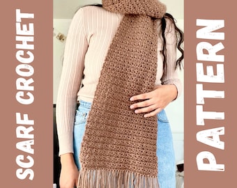 May include: A brown crocheted scarf with fringe. The scarf is worn by a person with a white sweater and blue jeans.