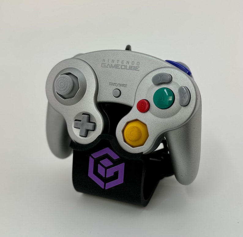 May include: A silver Nintendo GameCube controller with purple buttons and a black stand with a purple GameCube logo.