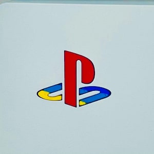 May include: A white PlayStation console with the PlayStation logo in red, blue and yellow.