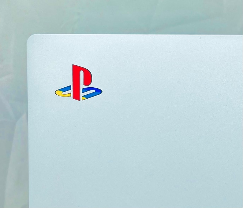 May include: A white surface with the PlayStation logo in red, blue, and yellow.