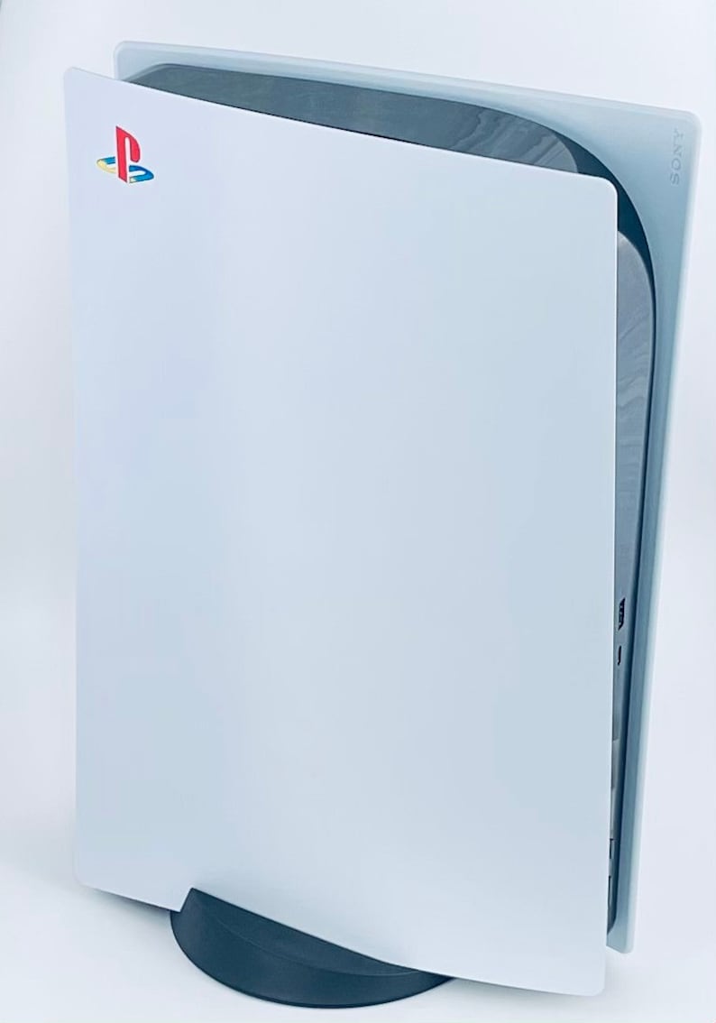 May include: A white PlayStation 5 console with the PlayStation logo on the front. The console is standing upright on a black base.