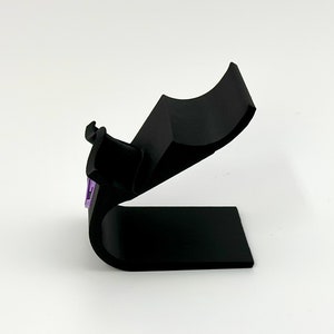 May include: A black plastic stand with a curved top designed to hold a phone or other device.
