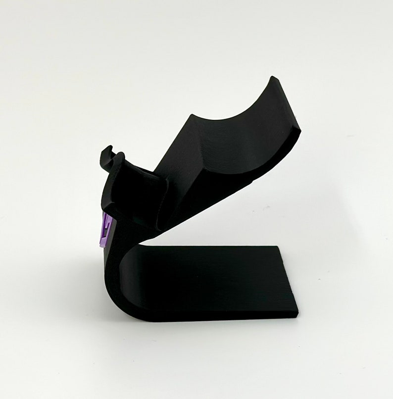 May include: A black plastic stand with a curved top designed to hold a phone or other device.