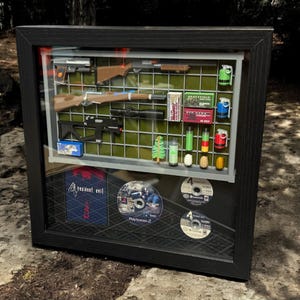 May include: A framed display of Resident Evil 4 video game memorabilia, including a game case, discs, and miniature weapons and items from the game.