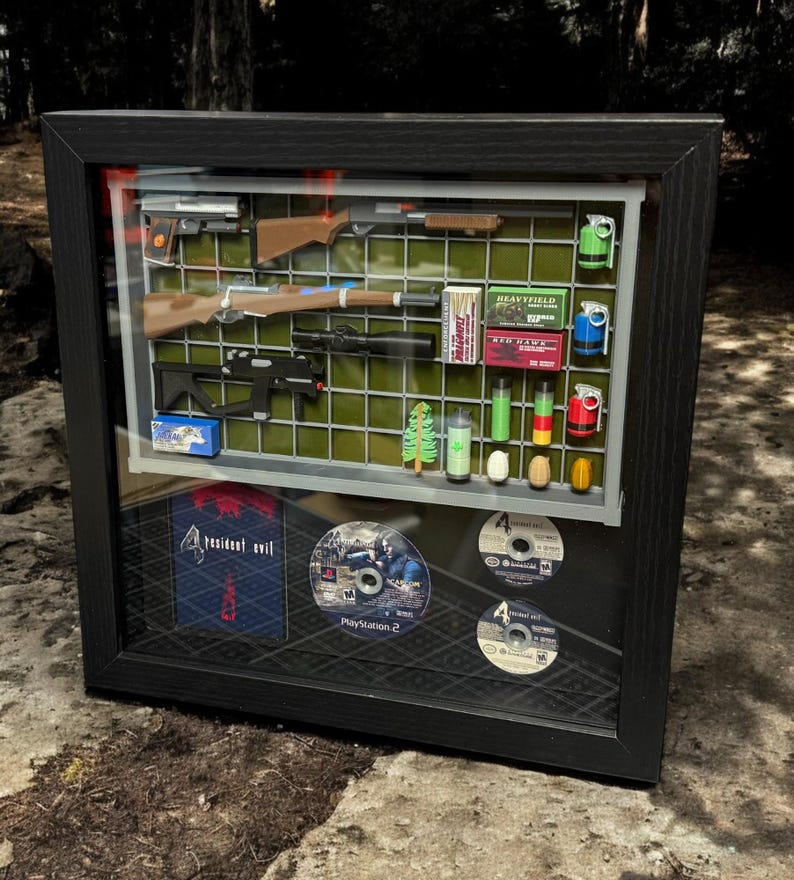 May include: A framed display of Resident Evil 4 video game memorabilia, including a game case, discs, and miniature weapons and items from the game.