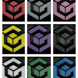 May include: Nine different colored 3D printed geometric shapes. Each shape is a cube with a smaller cube inside. The colors are red, gray, pink, yellow, purple, black, white, green, and blue.