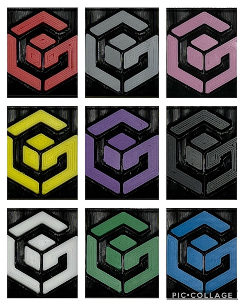 May include: Nine different colored 3D printed geometric shapes. Each shape is a cube with a smaller cube inside. The colors are red, gray, pink, yellow, purple, black, white, green, and blue.