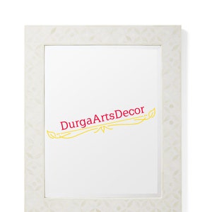 Puede incluir: Marco de fotos blanco con un patrón floral decorativo. El marco está hecho de hueso y tiene un fondo blanco. El texto "Durga ArtsDecor" está escrito en rojo y amarillo en el marco.