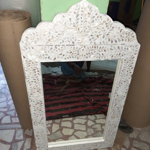 Puede incluir: Un espejo blanco con un marco decorativo de nácar. El marco presenta un diseño floral con hojas y un motivo central. El espejo es rectangular y tiene un borde biselado.