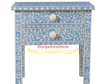May include: A light blue nightstand with two drawers and white bone inlay floral designs. The drawers have white knobs. The nightstand is made of wood and has a floral design on the legs.