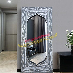 Puede incluir: Un espejo grande, rectangular y gris con un diseño blanco, ornamentado, en forma de hoja alrededor del marco. El espejo tiene una parte superior arqueada y una superficie reflectante. El texto "DurgaArtsDecor" es visible en el reflejo.