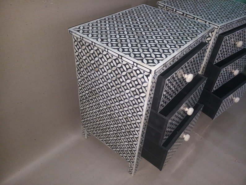 May include: A black and white bone inlay nightstand with three drawers. The drawers have black fronts and bone inlay handles. The nightstand has a geometric pattern.