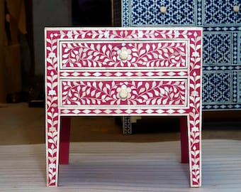 May include: A two-drawer nightstand with a pink base and white floral inlay. The drawers have white bone inlays and floral designs. The nightstand is made of wood and has a traditional style.