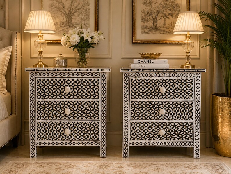 Bone inlay Two white bedside tables with three drawers each. The drawers feature black and white geometric patterns and white knobs. The bedside tables are made of wood and have a distressed finish.