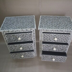 May include: Two white and black patterned bedside tables with three drawers each. The drawers have white knobs.