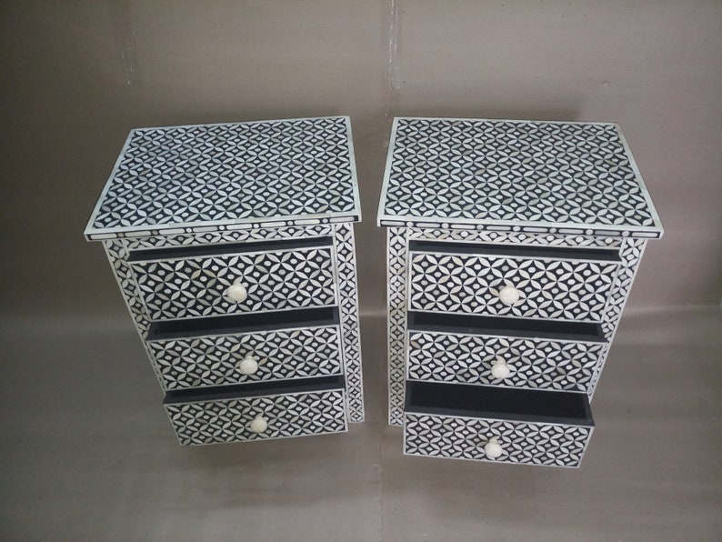 May include: Two white and black patterned bedside tables with three drawers each. The drawers have white knobs.
