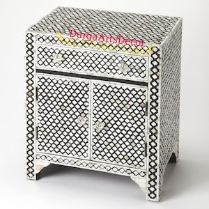 Puede incluir: Una mesita de noche negra y blanca con un patrón geométrico hecho de incrustaciones de hueso. La mesita de noche tiene un cajón y dos puertas.