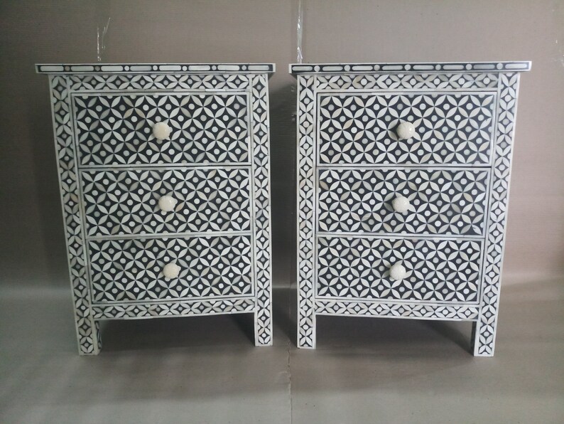 May include: Two black and white nightstands with three drawers each. The drawers have a geometric pattern and white knobs. The nightstands are made of wood and have a traditional style.
