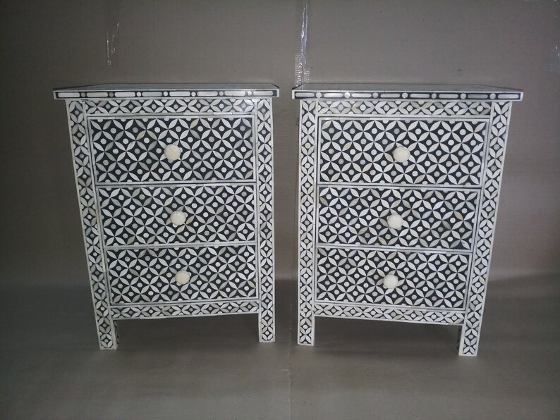 May include: Bone inlay Two white and black geometric patterned bedside tables with three drawers each. The drawers have white knobs.