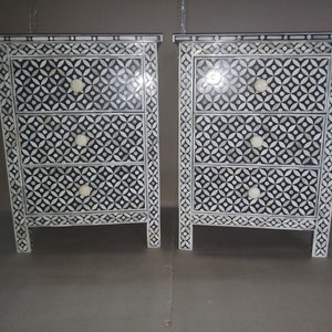 May include: Two black and white nightstands with intricate geometric patterns made of bone inlay. Each nightstand has three drawers with white knobs.