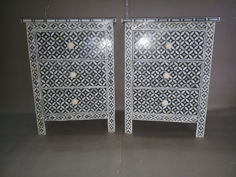 May include: Two black and white nightstands with intricate geometric patterns made of bone inlay. Each nightstand has three drawers with white knobs.