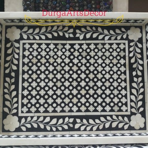 K&ouml;nnte beinhalten: Ein rechteckiges Serviertablett mit einem geometrischen Muster in Schwarz und Wei&szlig; aus Knocheninlay. Das Tablett hat einen dekorativen Rand mit floralen Motiven.