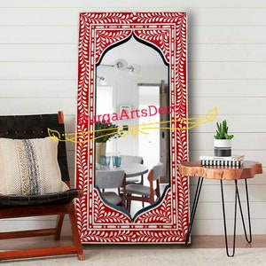 Puede incluir: Un espejo de incrustaciones de hueso rojo y blanco con un diseño floral decorativo. El espejo tiene una parte superior arqueada y está enmarcado en un marco rectangular.