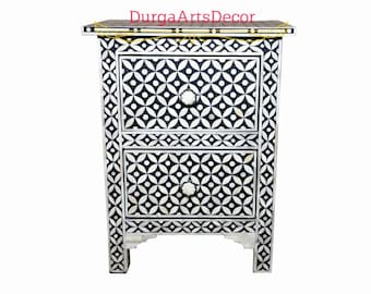 May include: A black and white bone inlay nightstand with two drawers and a geometric pattern. The nightstand has a decorative design on the front and sides.
