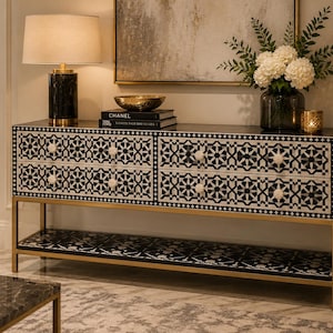 May include: A rectangular console table featuring four drawers with a black and white geometric inlay pattern, round white knobs, and a lower shelf with a matching inlay design, all supported by a gold-toned metal frame with four straight legs.