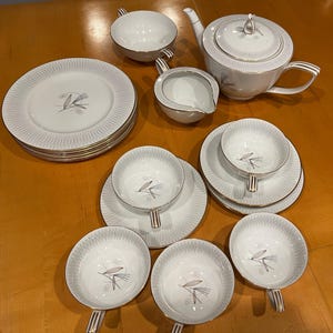 May include: A white tea set with a gold trim and a delicate floral design. The set includes a teapot, creamer, sugar bowl, and six cups and saucers.