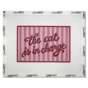 May include: A needlepoint canvas featuring a pink and white vertical striped background with the dark red text the cat is in charge centred in the middle. The canvas has a white border with the repeating text Birch NDLPT printed on it.