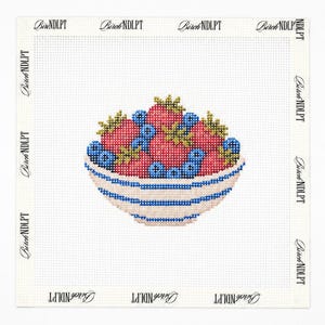 May include: A needlepoint canvas featuring a bowl filled with red strawberries and blue blueberries. The bowl is white with horizontal blue stripes. The text Birch NDLPT is printed repeatedly along the white border of the square canvas.