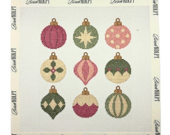 May include: A square needlepoint canvas featuring nine distinct Christmas ornament designs arranged in a grid. Each ornament is rendered in cross-stitch style with varied patterns in shades of pink, green, and cream. The text Birch NDLPT is printed along the white border.