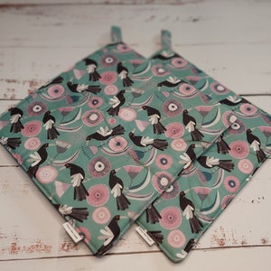 May include: A pair of teal blue pot holders with a black and white bird and pink flower pattern.